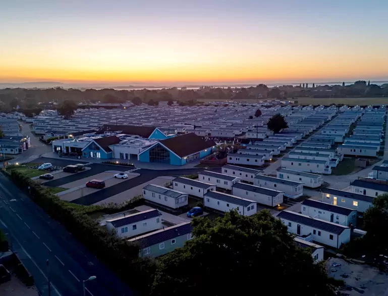 An aerial view of a large holiday park filled with static caravans under a beautiful sunset sky, showcasing the layout of the park and main buildings, Hayling Island.