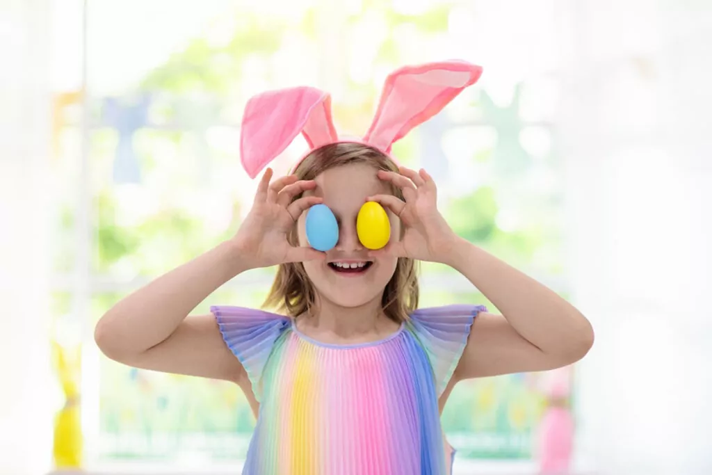 Child wearing bunny ears holding colourful Easter eggs over their eyes during a fun seasonal activity at Hayling Island