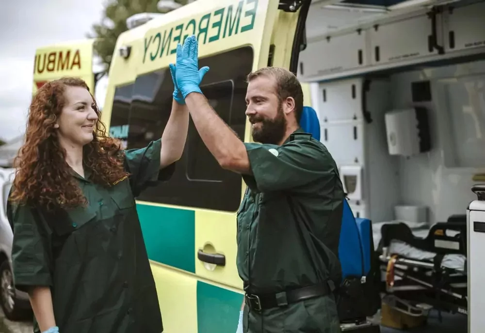 Emergency service workers standing beside an ambulance celebrating with a high five while representing blue light staff offers at Hayling Island.