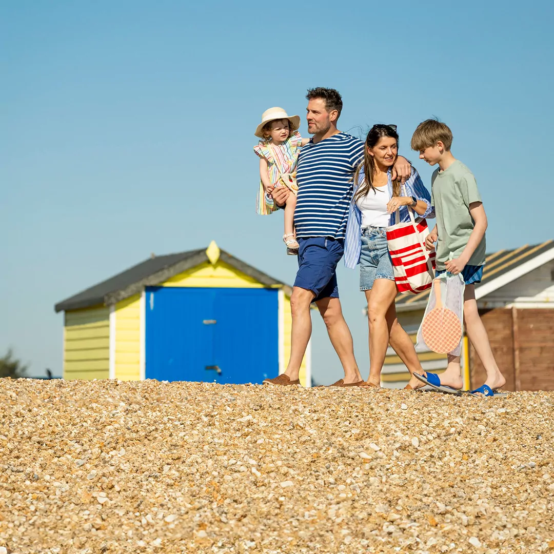 Family walking together along the pebble beach past colorful beach huts near Meadow Bay Villages Hayling Island