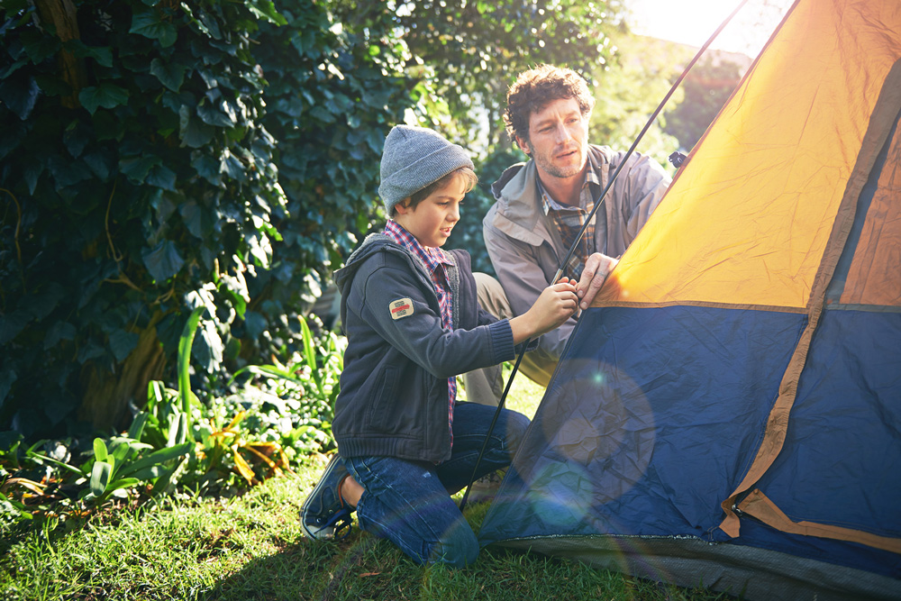 A father and son working together to pitch a blue and orange tent for a camping trip at Henfold Lakes.