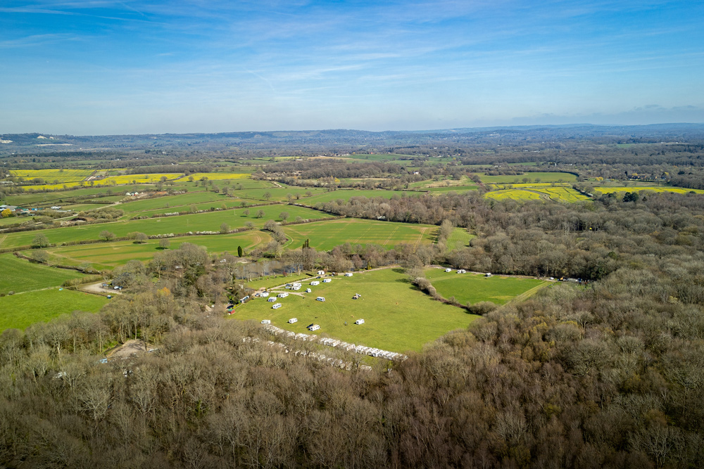 High-angle aerial view of the lush green countryside and camping fields at Henfold Lakes.