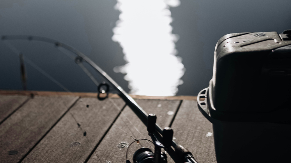 Close-up view of a fishing rod and reel resting on a wooden jetty by the water's edge at Henfold Lakes.