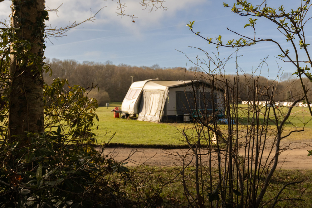A touring caravan with an attached awning parked on a spacious grass pitch at Henfold Lakes.