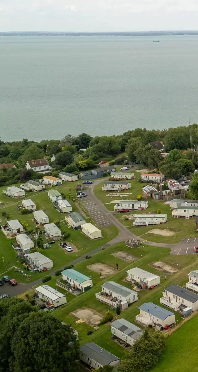 Aerial shot of static caravans nestled in green surroundings by the sea at Hollybush Farm, part of Meadow Bay Villages.