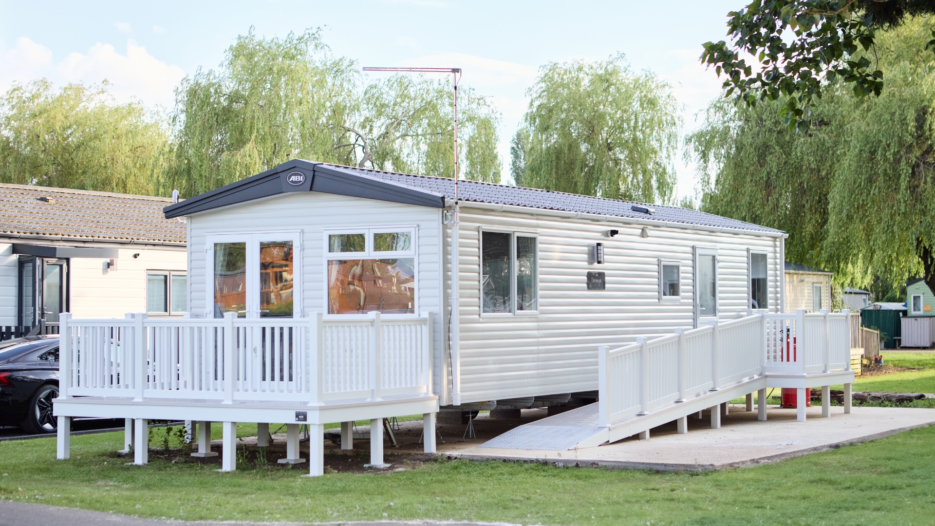 Accessible static caravan at Meadow Bay Villages, featuring a white deck and ramp for wheelchair access, set in a peaceful, green park setting.