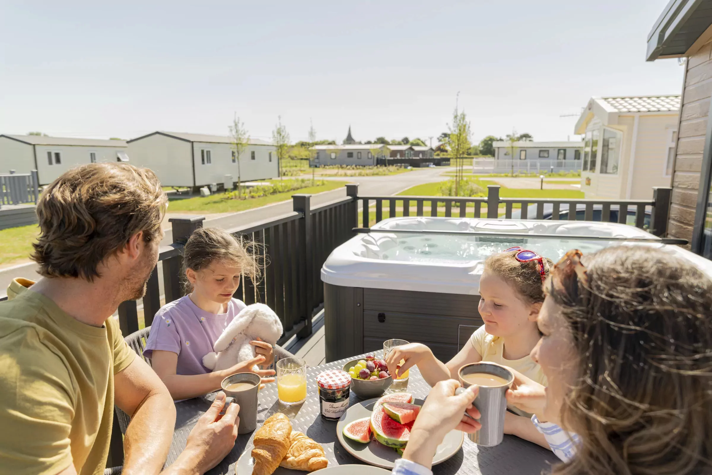 Family enjoying a sunny breakfast on the decking beside a hot tub at Hayling Island holiday park