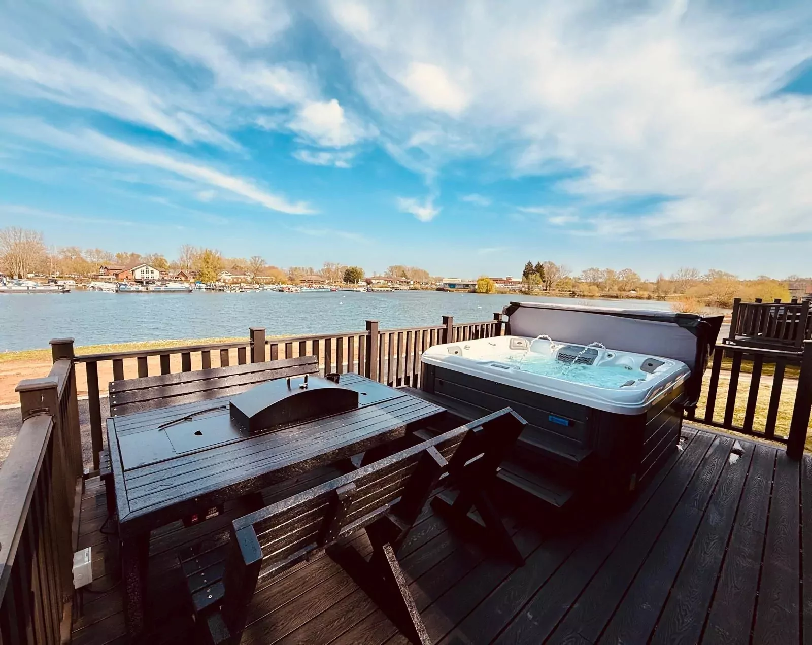Private deck with hot tub and outdoor dining area overlooking a tranquil lake at a luxury holiday lodge in Meadow Bay Villages.