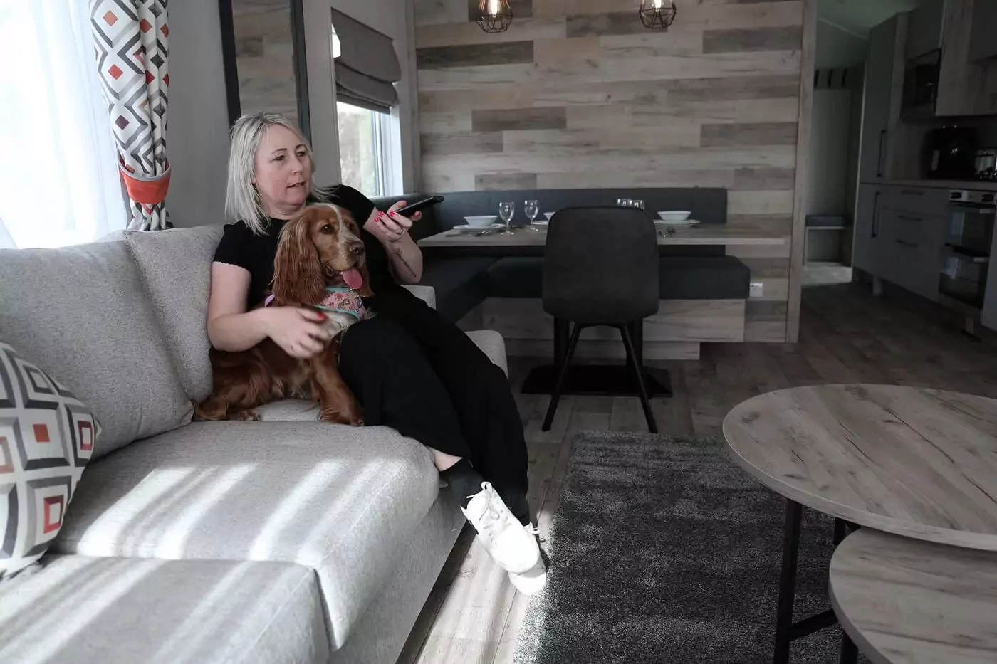 Woman relaxing with her brown spaniel dog on a sofa inside a modern, pet-friendly static caravan featuring a contemporary open-plan interior.