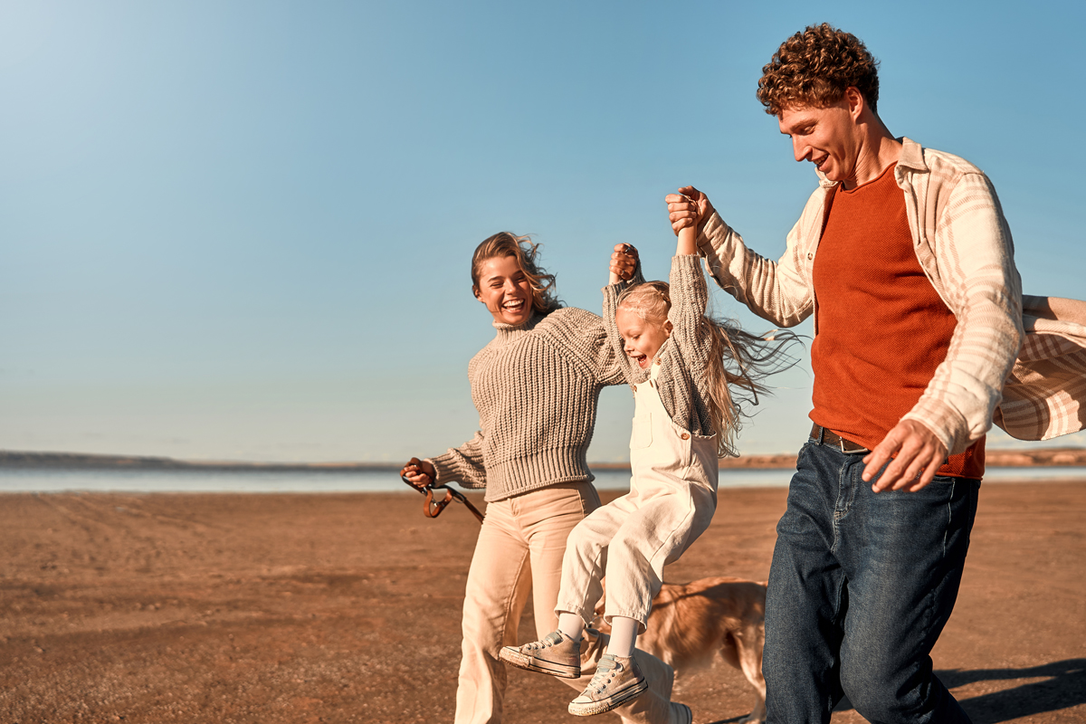 Happy family playing together on a sandy beach, lifting their child between them on a sunny day at Meadow Bay Villages.