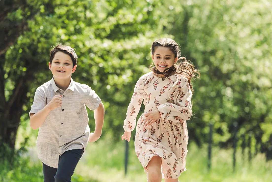 Two happy children running and playing in a lush green park setting at Meadow Bay Villages.