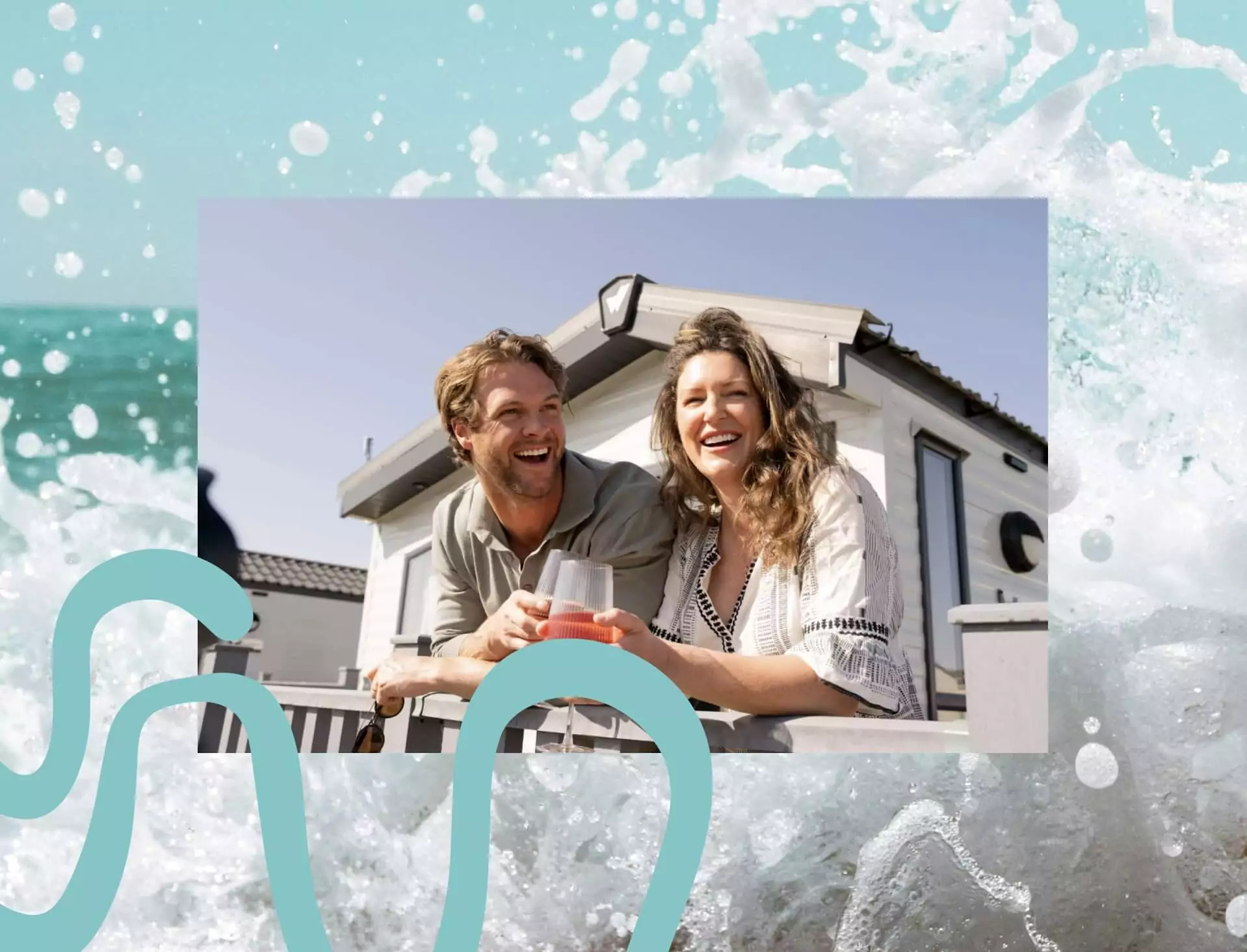 Smiling couple relaxing with drinks on the decking of a modern static caravan at a sunny holiday park.