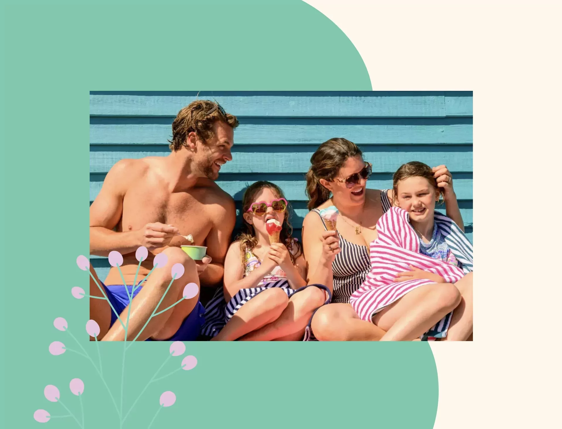 Happy family sitting against a blue beach hut wall, enjoying ice creams and snacks in swimwear and striped towels on a sunny summer day.