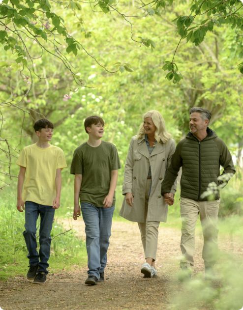 Family strolling along a leafy woodland trail, smiling and talking.