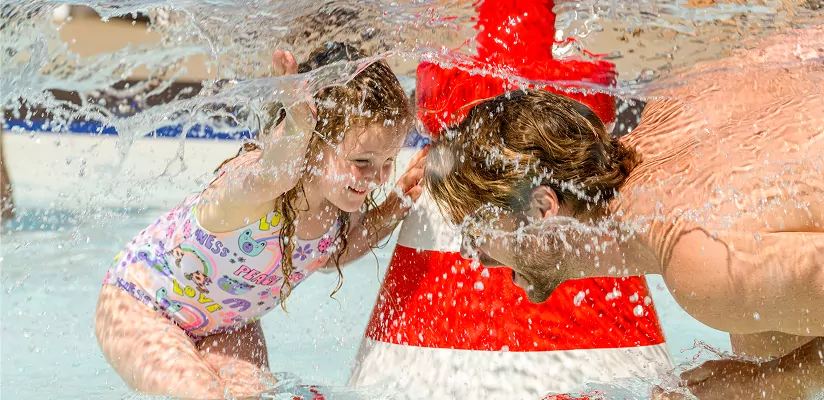 Adult and child laughing together while playing in an outdoor splash area at Meadow Bay Villages