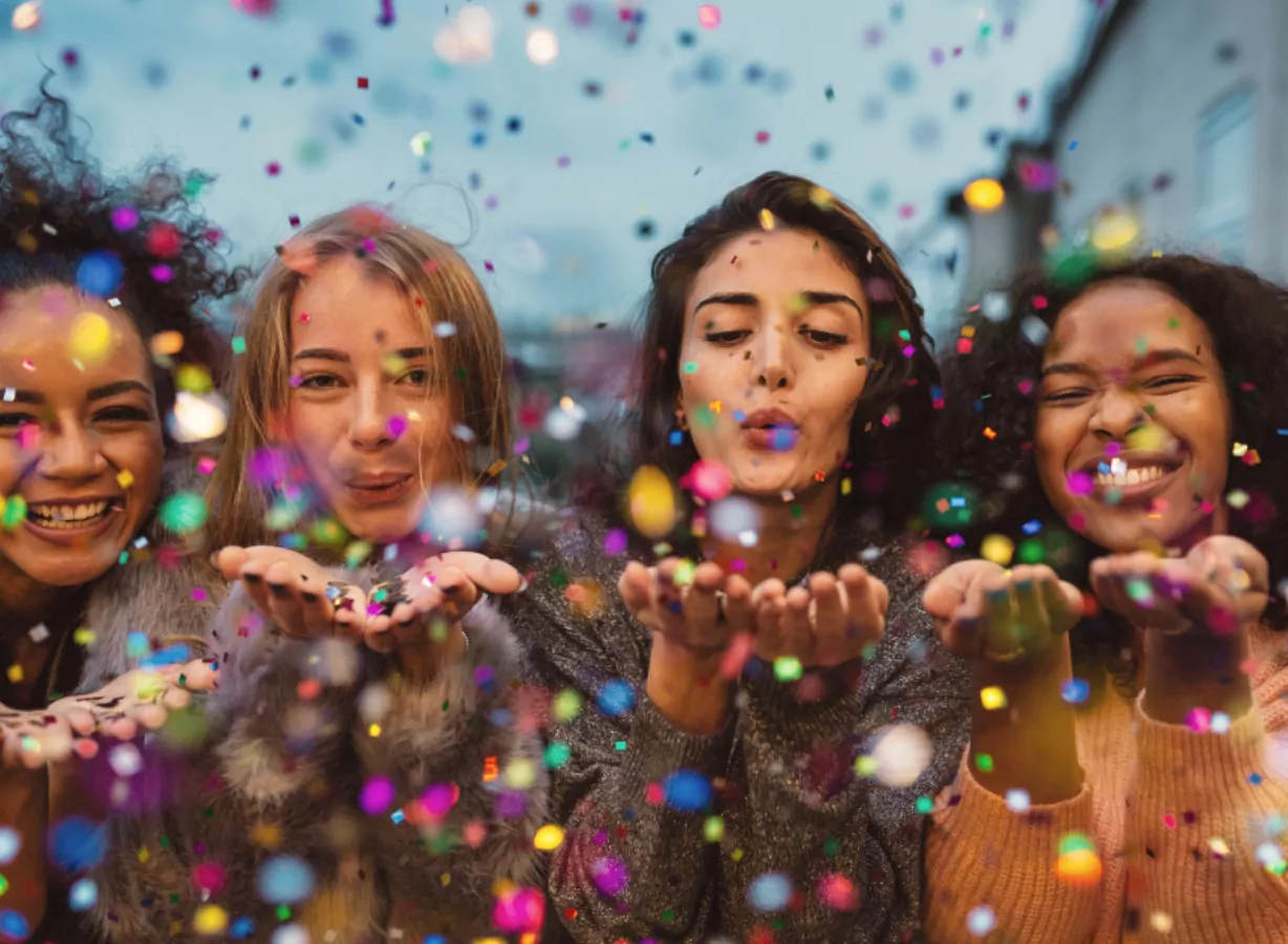 Group of friends celebrating outdoors as colourful confetti falls during a vibrant festival event, Meadow Bay Villages