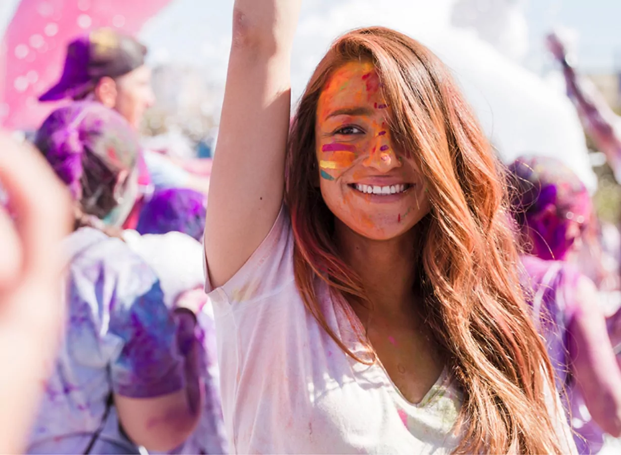 Smiling woman covered in bright powder paint enjoying a lively outdoor summer celebration, Meadow Bay Villages