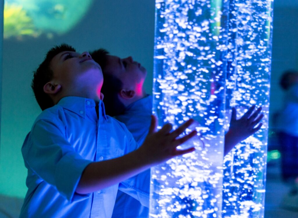 Child exploring a calming sensory room with illuminated bubble columns designed for relaxation and stimulation, Meadow Bay Villages