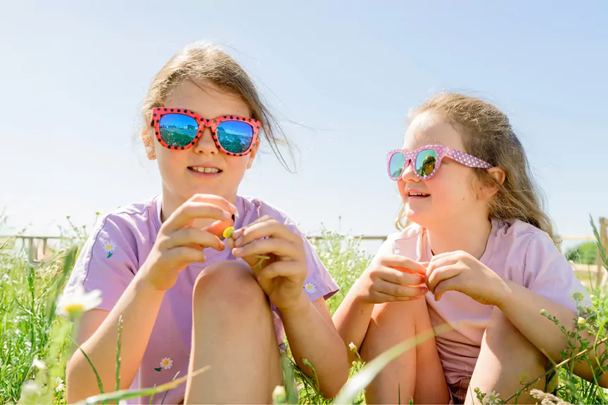 Two young girls wearing colorful sunglasses sitting in a sunny wildflower meadow, Meadow Bay Villages