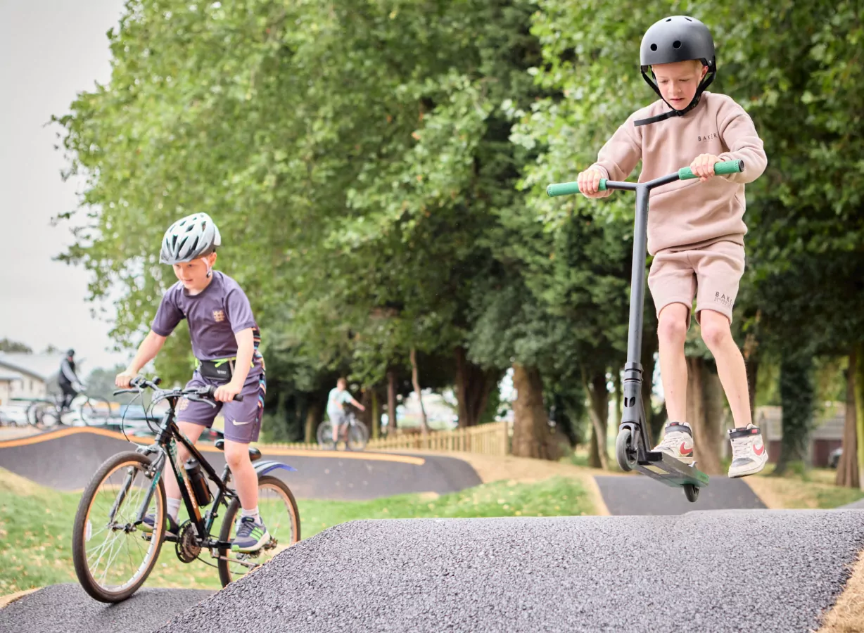 Children riding bikes and scooters along a pump track obstacle course in the park activity area, Meadow Bay Villages.