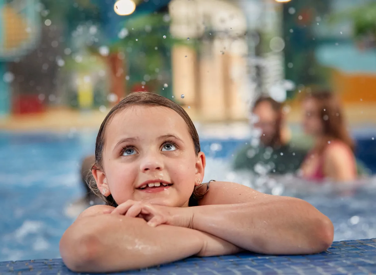 Child enjoying time in the indoor swimming pool with water splashing during a family swim session, Meadow Bay Villages.