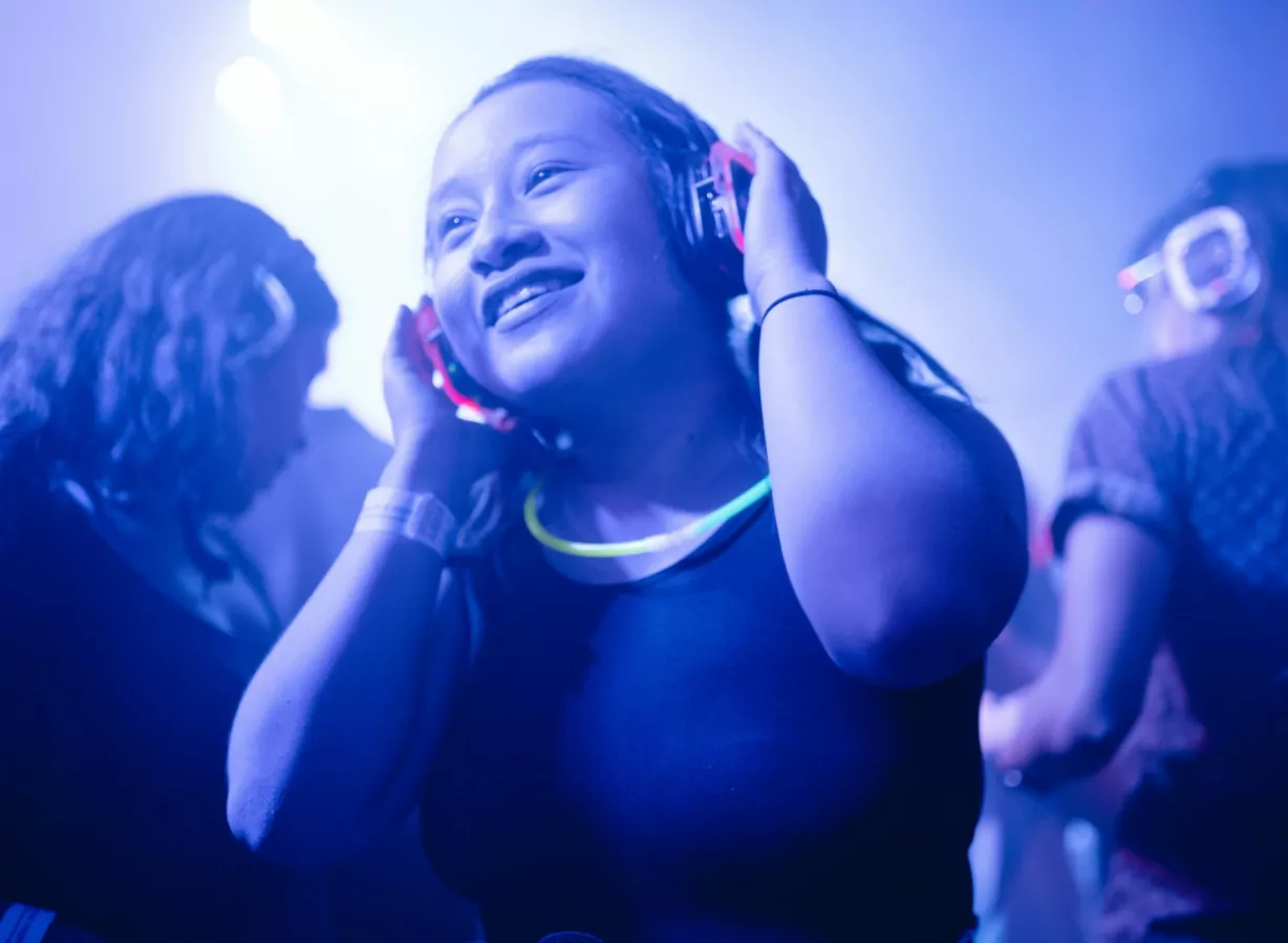 Young guest enjoying music through headphones at a lively silent disco event with colourful lighting, Meadow Bay Villages.