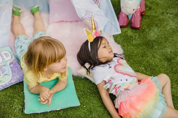 Two young children lying on the grass next to a unicorn play tent during a themed activity, Meadow Bay Villages