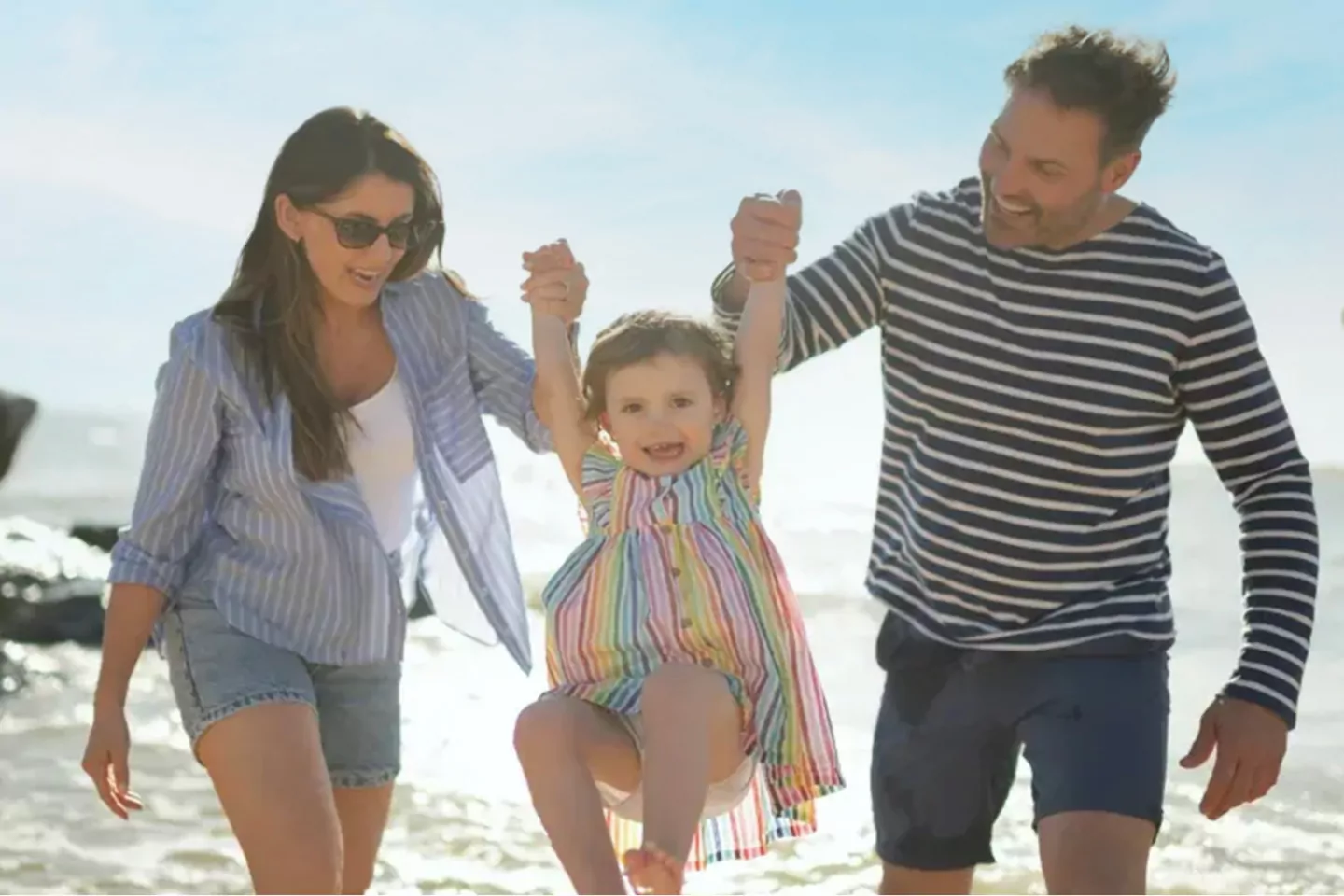 A happy family playing on the shore and lifting their young daughter into the air at the beach, Meadow Bay Villages