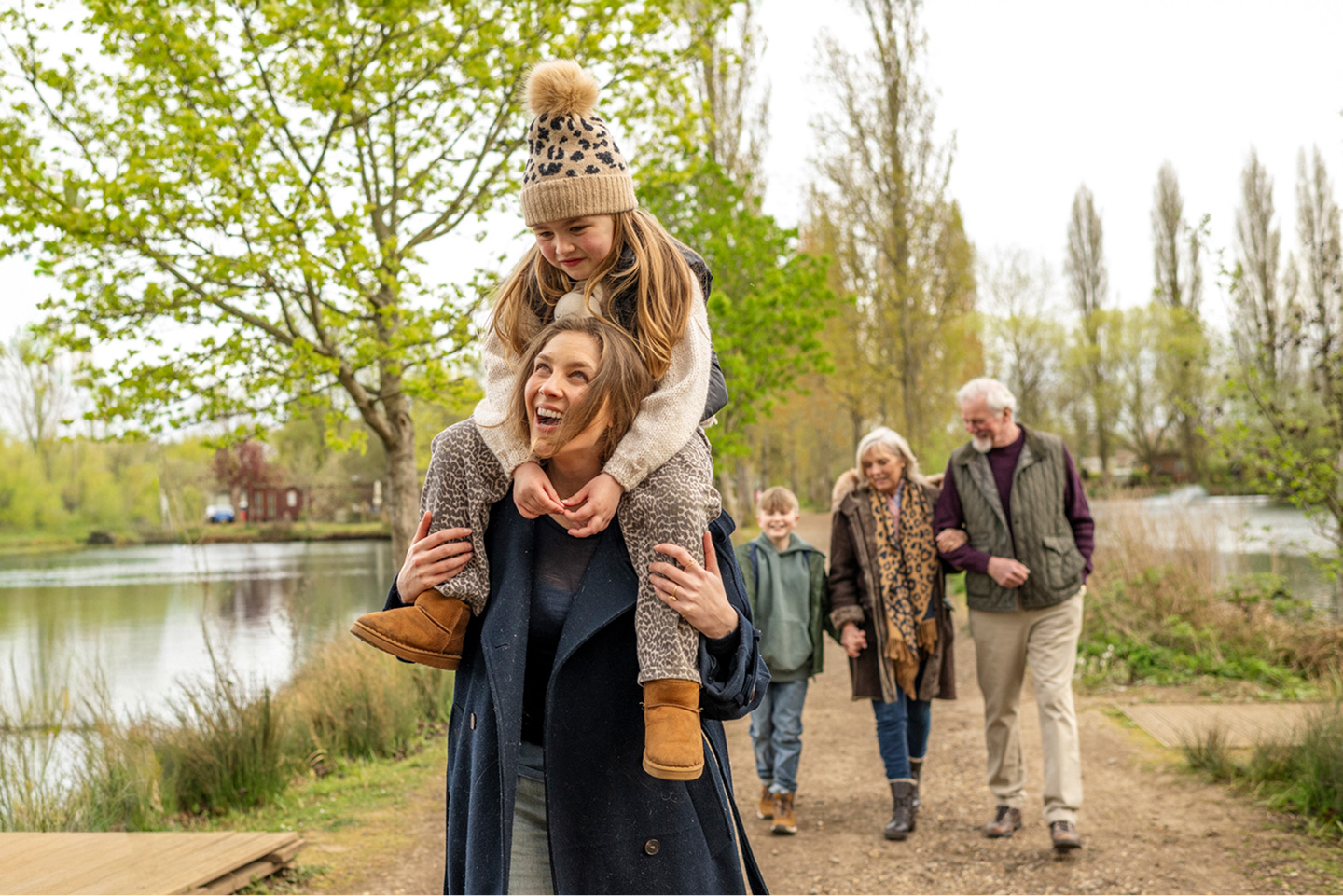 Mother giving daughter a piggyback ride on a family walk by the lake