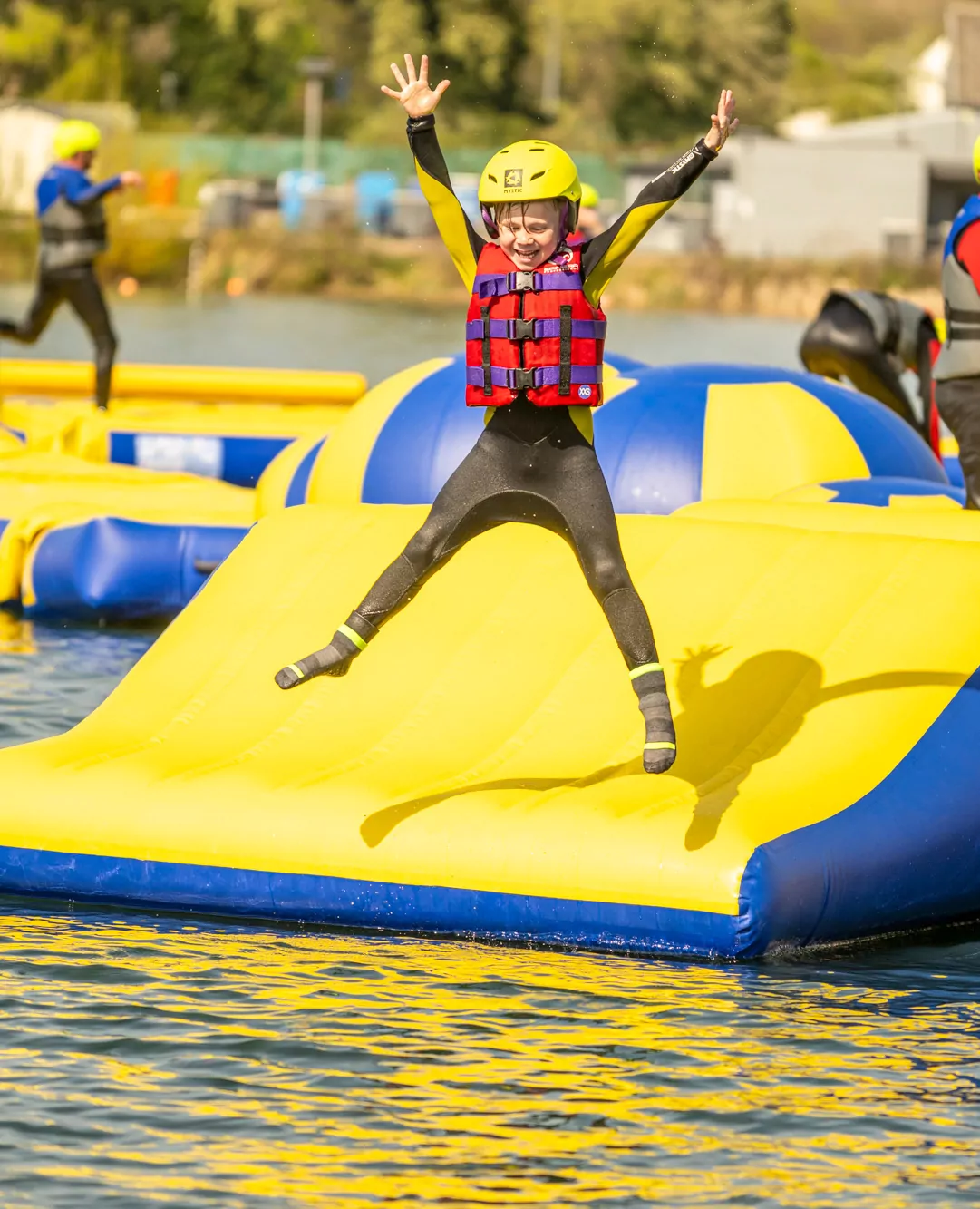 Child enjoying the inflatable aqua park while wearing a helmet and buoyancy aid at Billing Aquadrome.