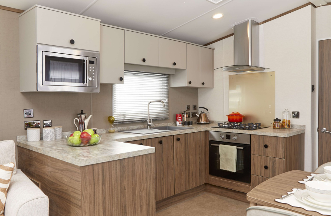 Modern caravan kitchen with integrated appliances and wood-effect cabinetry at Meadow Bay Villages