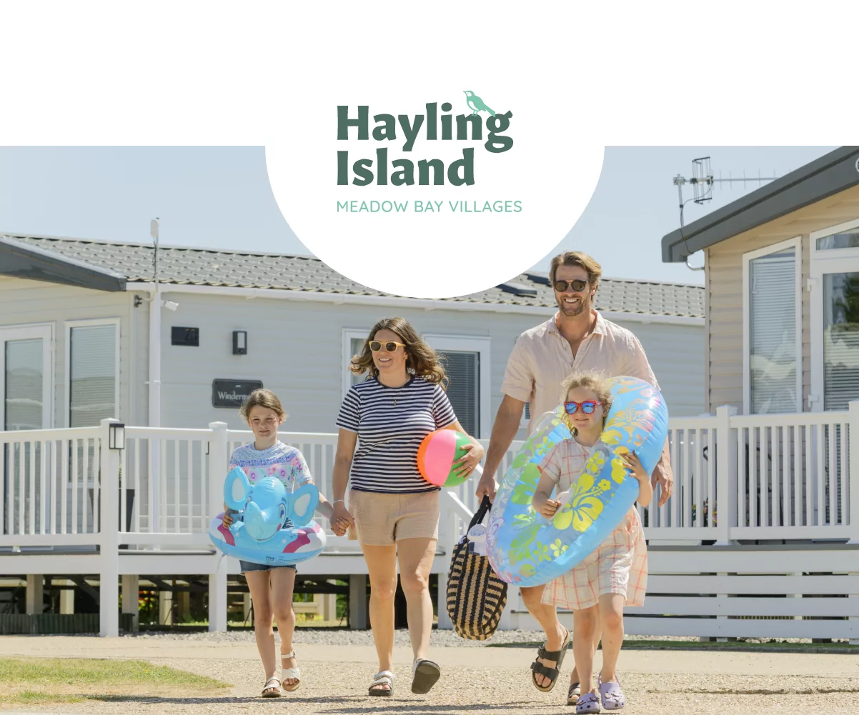 Happy family walking through a holiday park with beach gear and floaties at Hayling Island, Meadow Bay Villages.