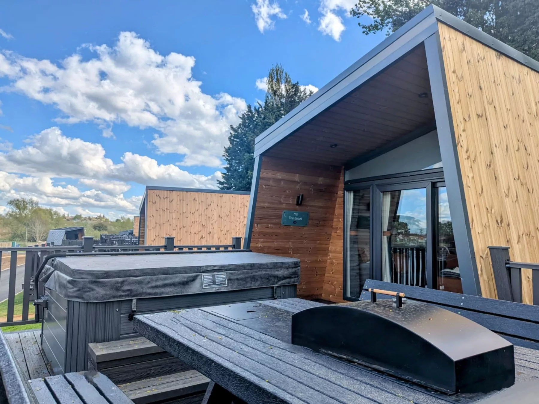 Contemporary wooden lodge with private hot tub and outdoor dining area at Meadow Bay Villages, perfect for a relaxing break.