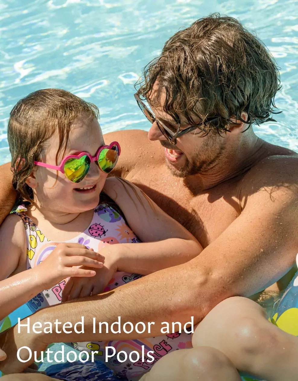 A father and daughter smiling and playing together in the outdoor swimming pool at Meadow Bay Villages.