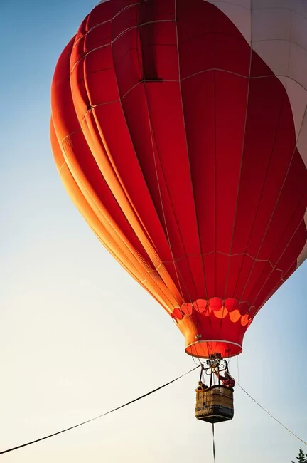 A red and white hot air balloon floats in a blue sky.