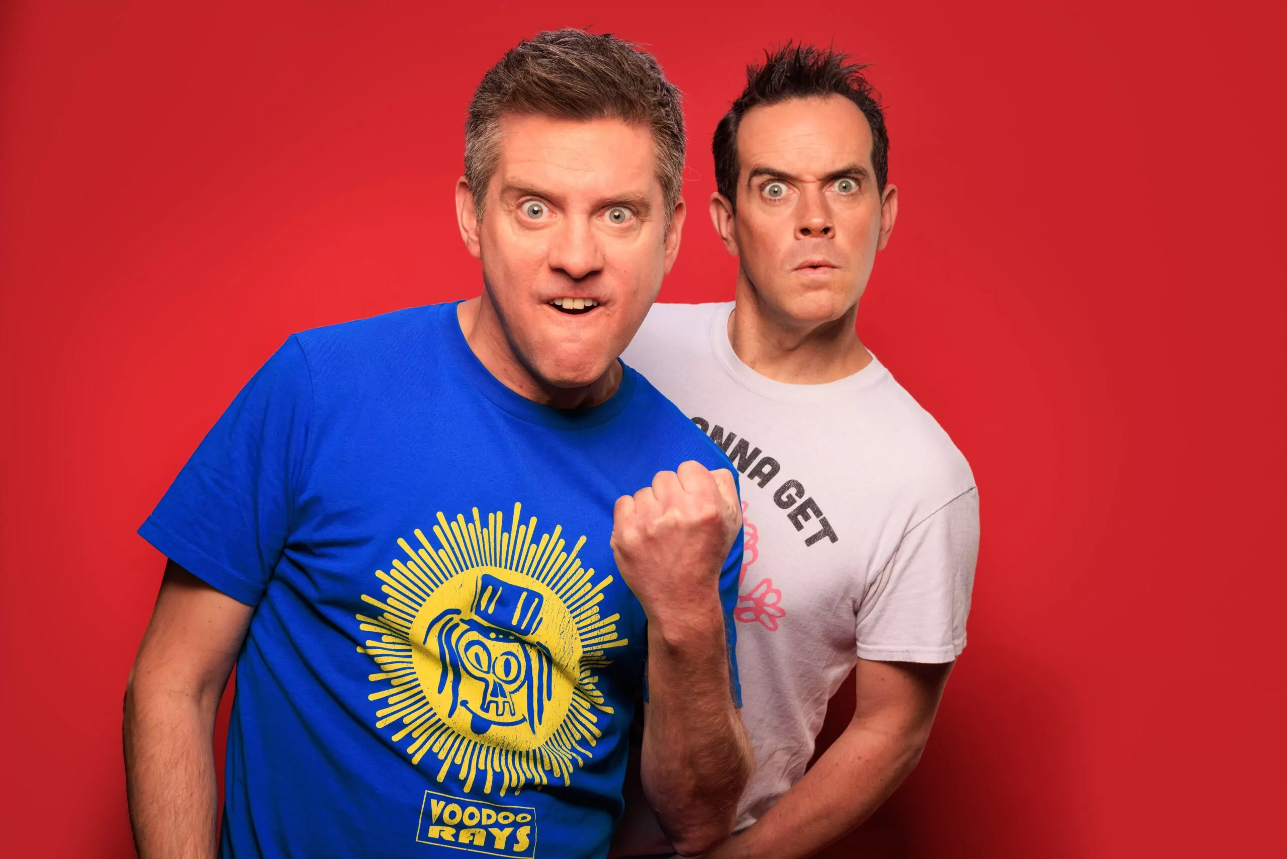 Two men make funny faces against a red background.
