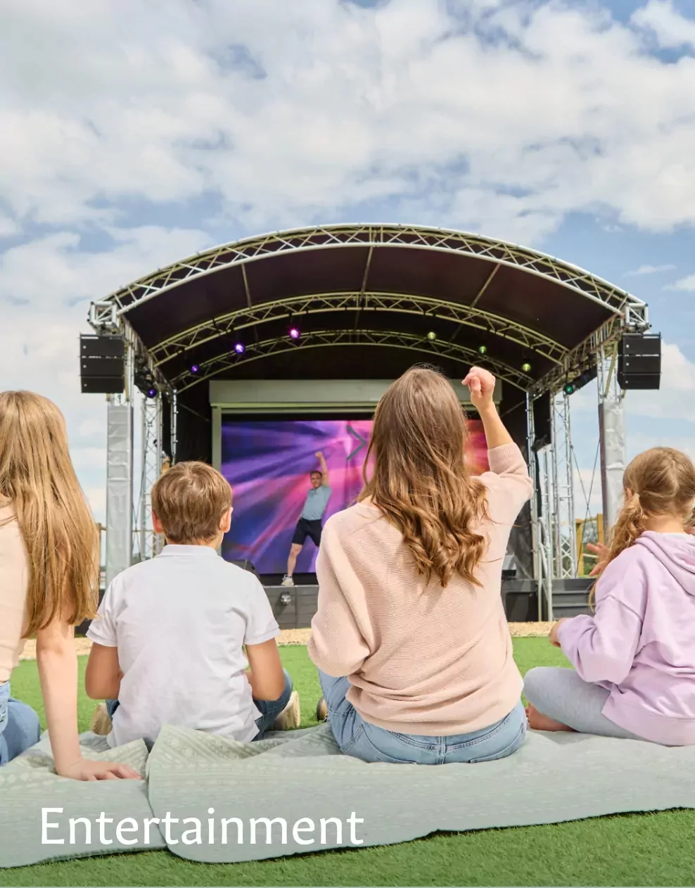 Families sitting on blankets watching a live outdoor stage performance at Meadow Bay Villages.