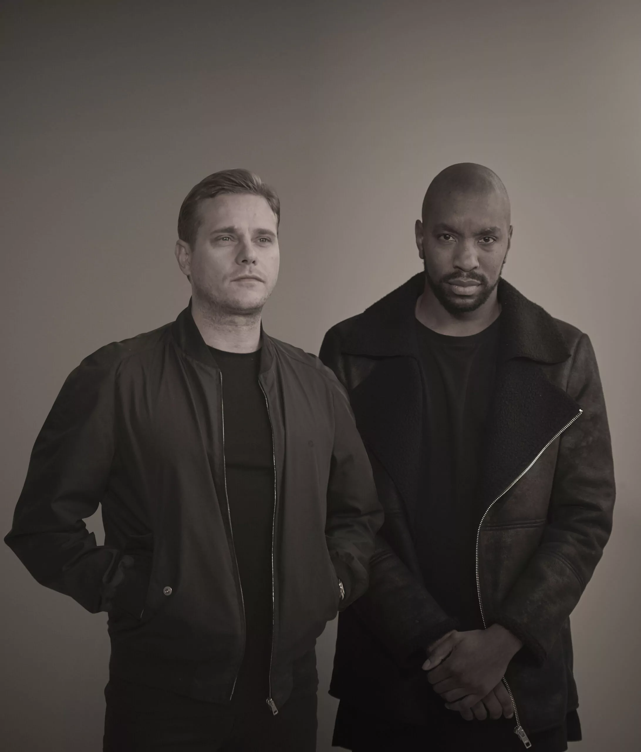 Two men in dark jackets pose in a black and white photo.