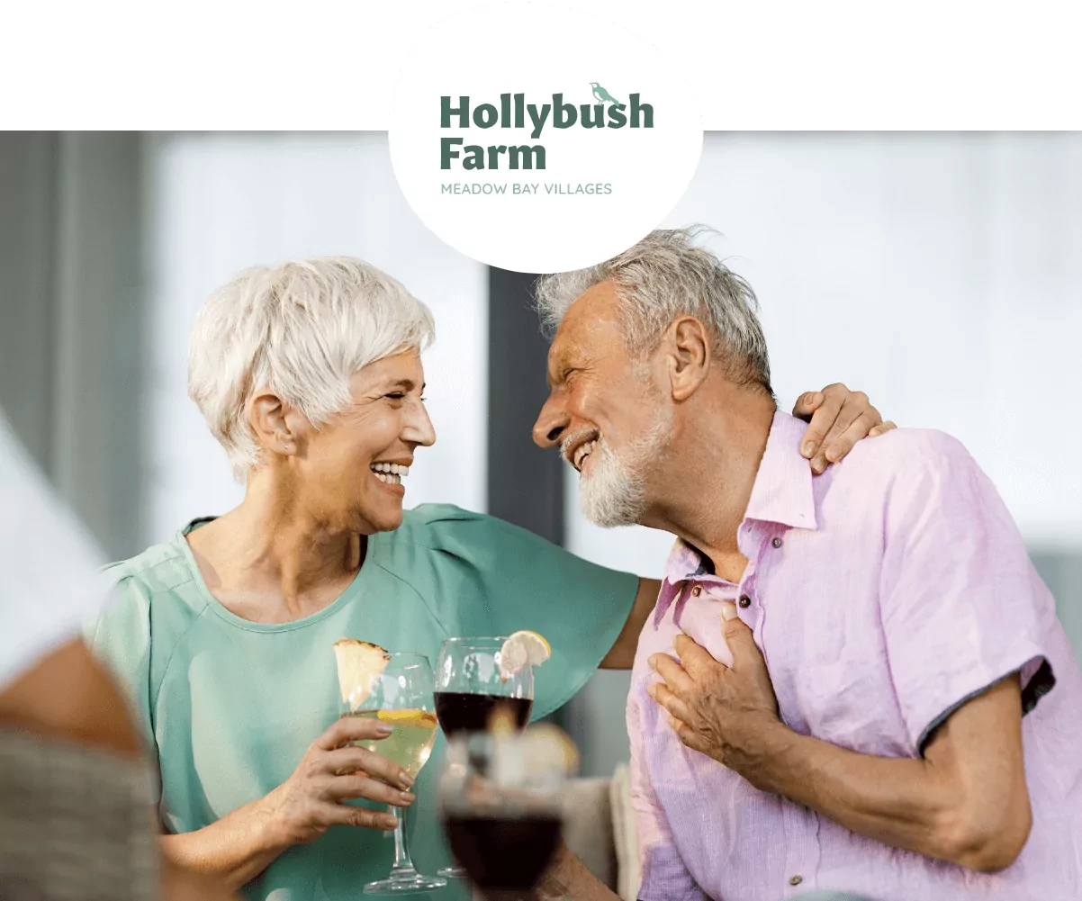Smiling older couple enjoying drinks and laughter together at Hollybush Farm holiday village.