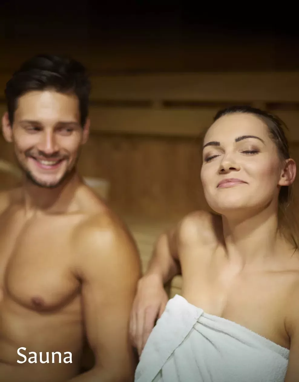 A couple relaxing and smiling in a warm wooden sauna, enjoying a soothing heat session at Meadow Bay Villages.