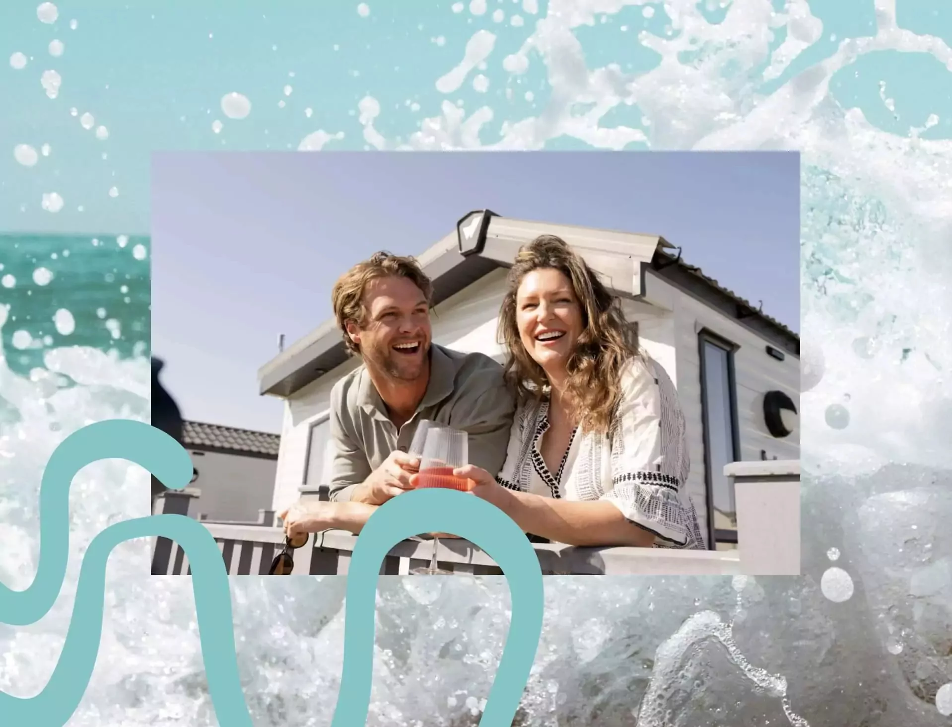 Smiling couple relaxing with drinks on the decking of a modern static caravan at a sunny holiday park.